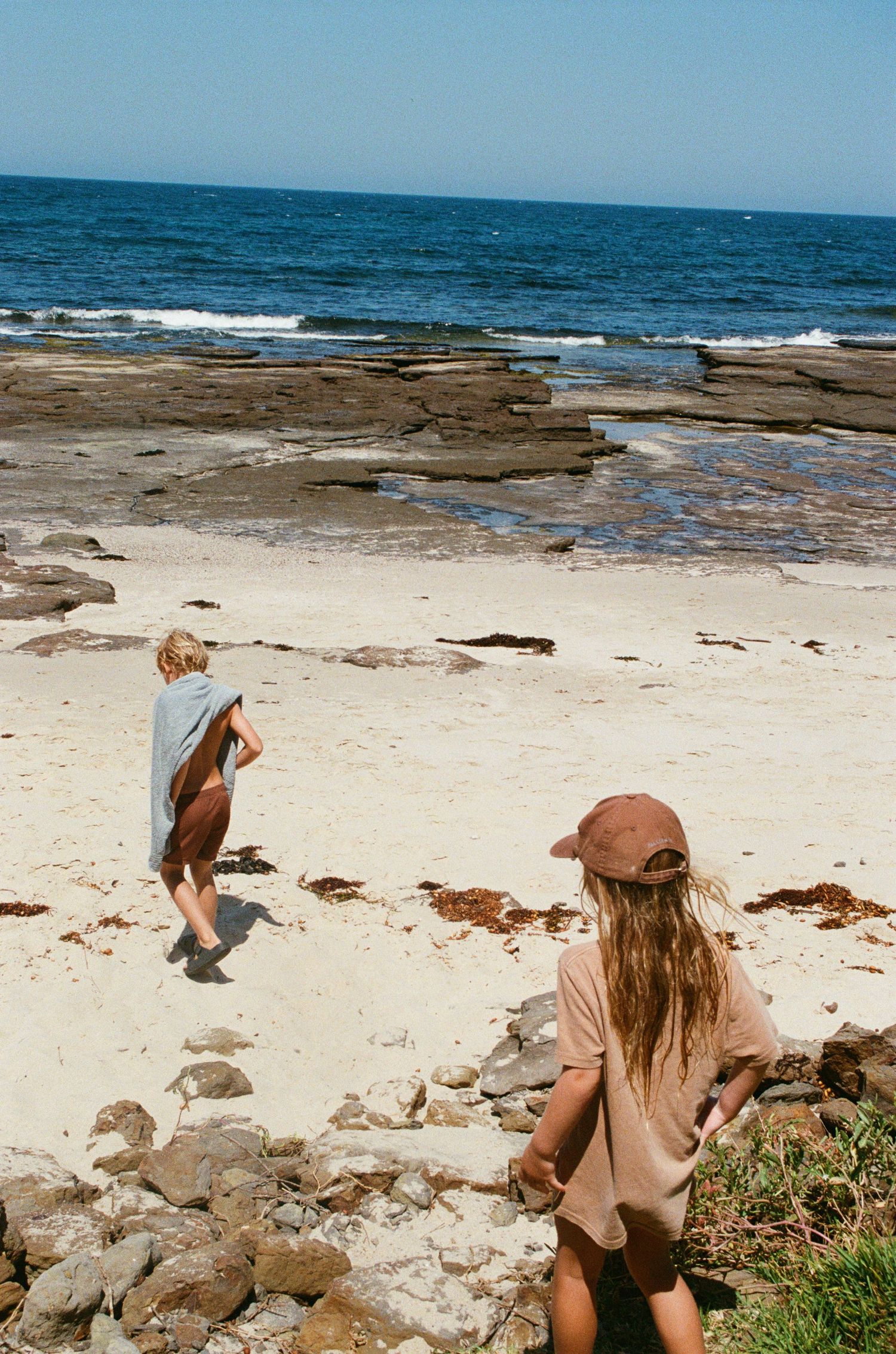 People explore a rocky coastal beach with waves crashing against the shore on a sunny day.