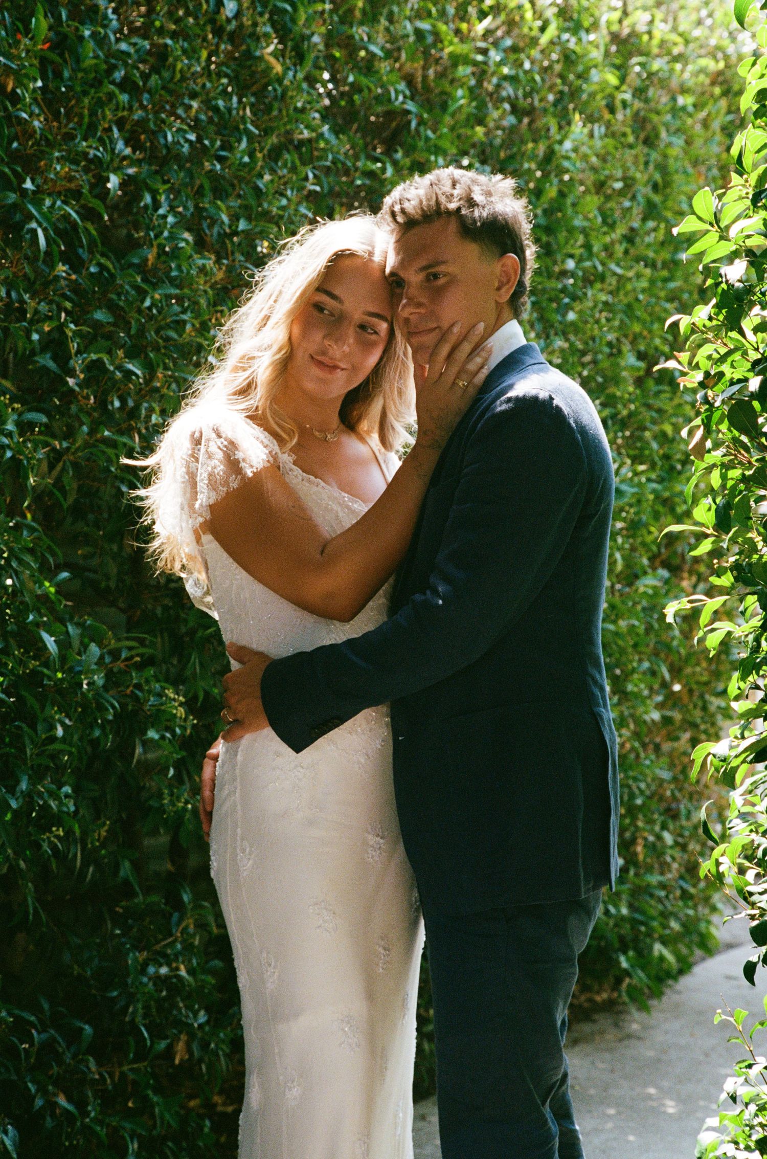 A tender wedding moment photographed against lush green foliage in natural lighting.