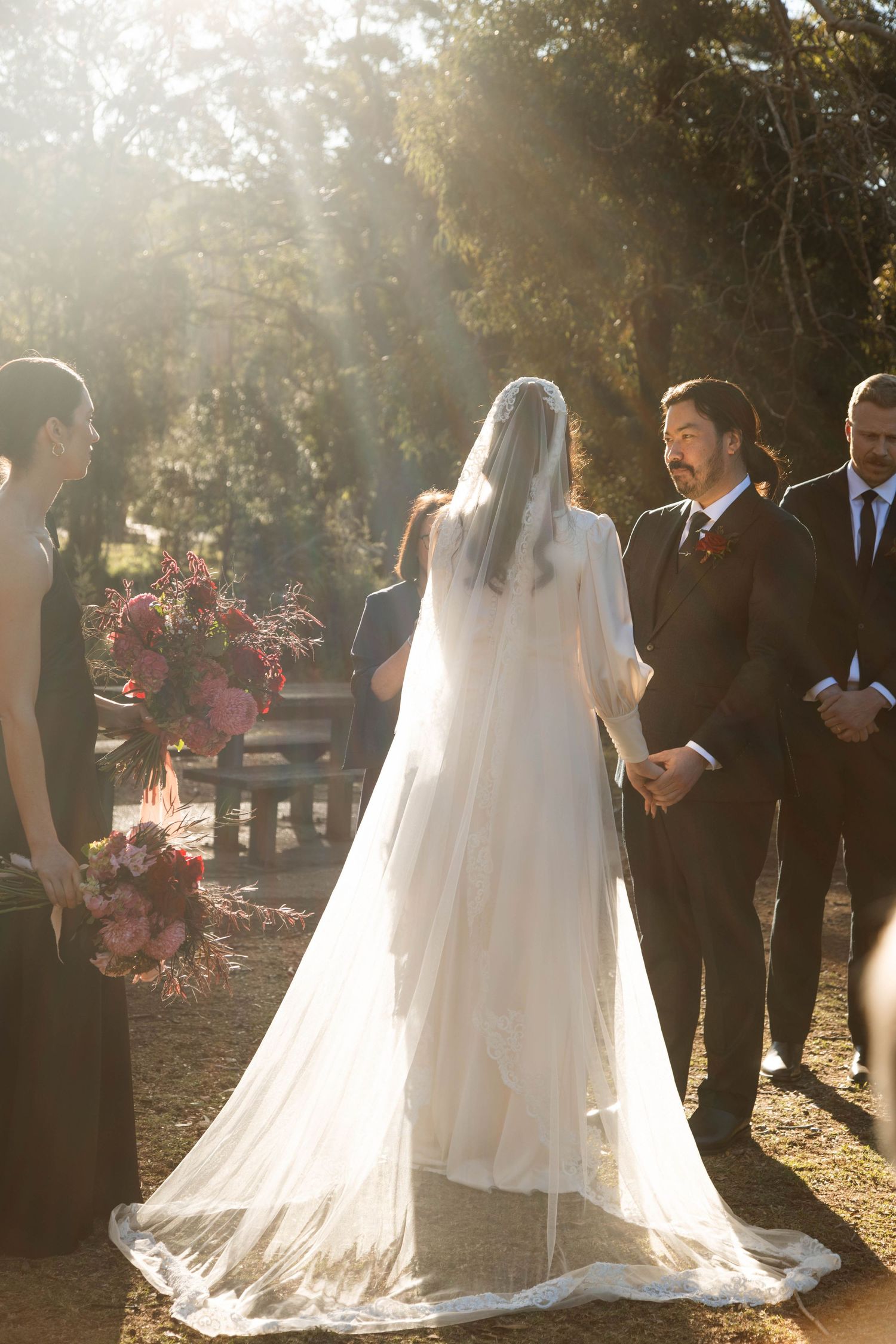 Golden hour wedding ceremony with flowing white dress and guests silhouetted against setting sun.