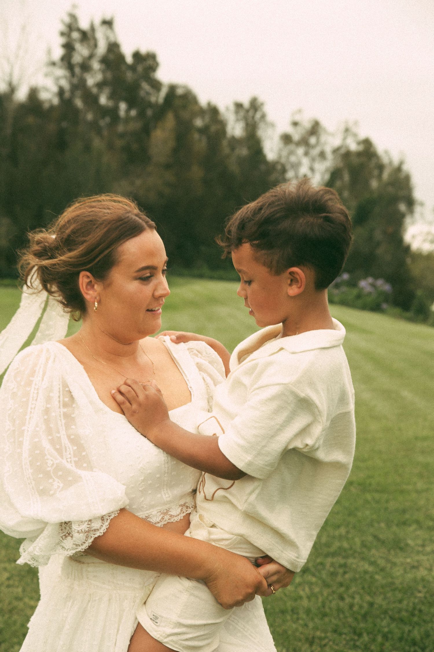 A tender moment captured on a grassy hillside with trees in the background.