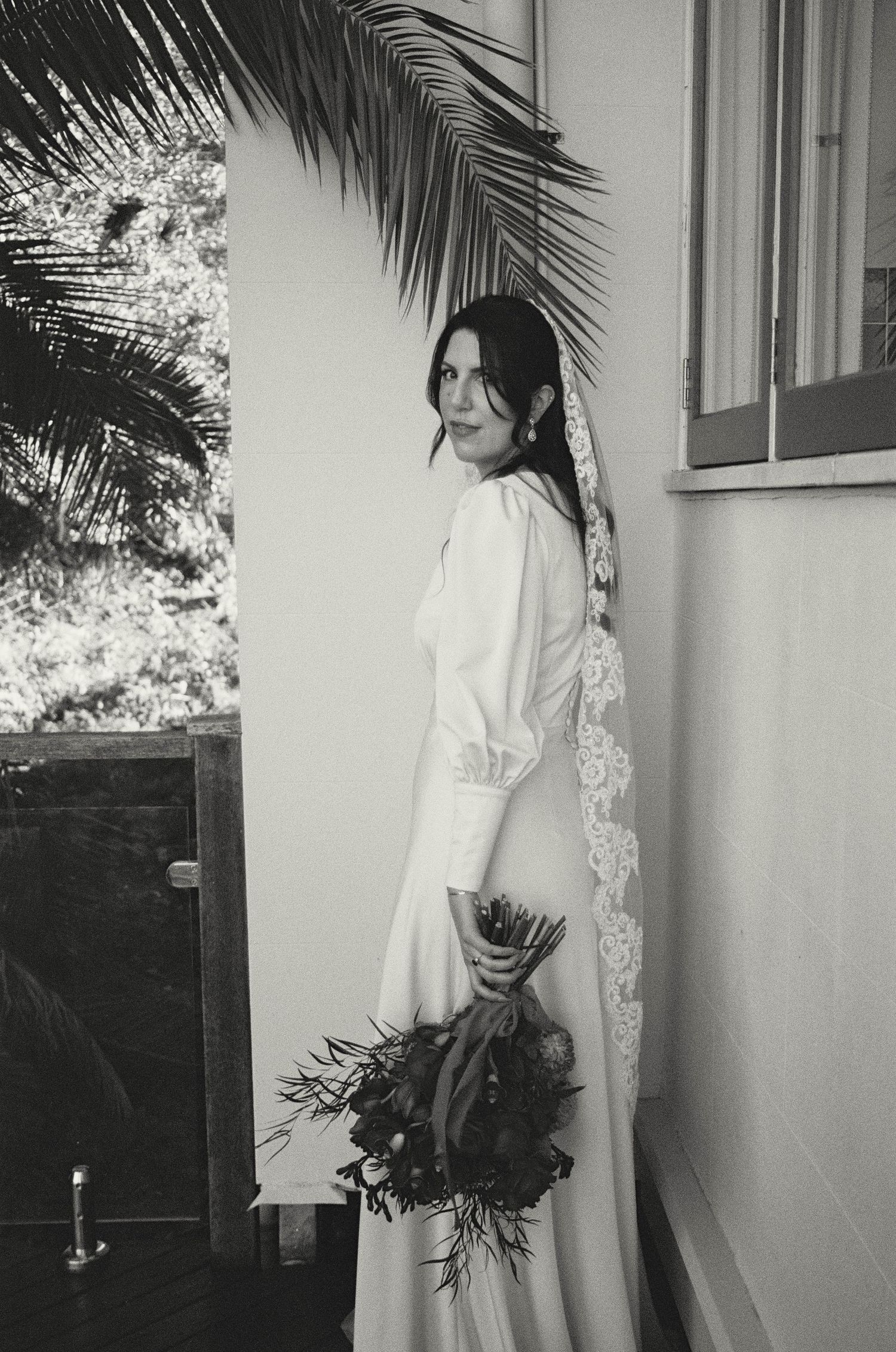 A black and white photo shows someone in a flowing white wedding dress holding flowers in an indoor setting.