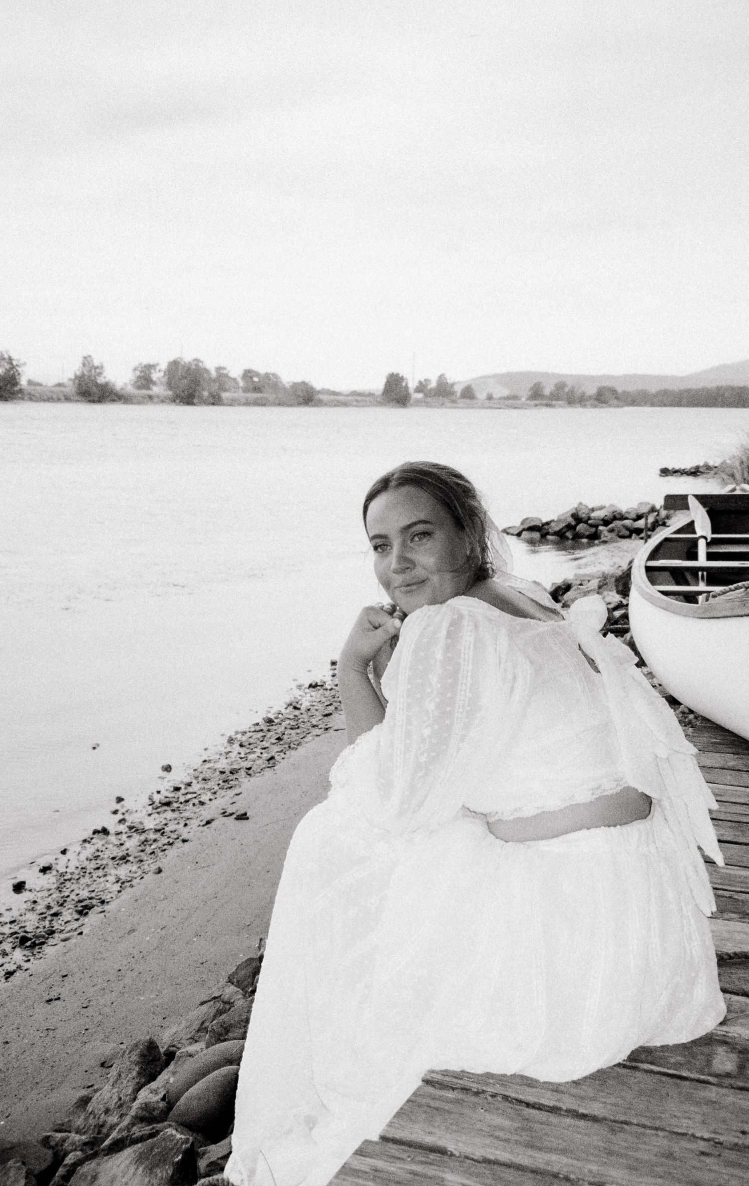 Ethereal black and white photos of flowing white dresses by a waterfront on a misty day.