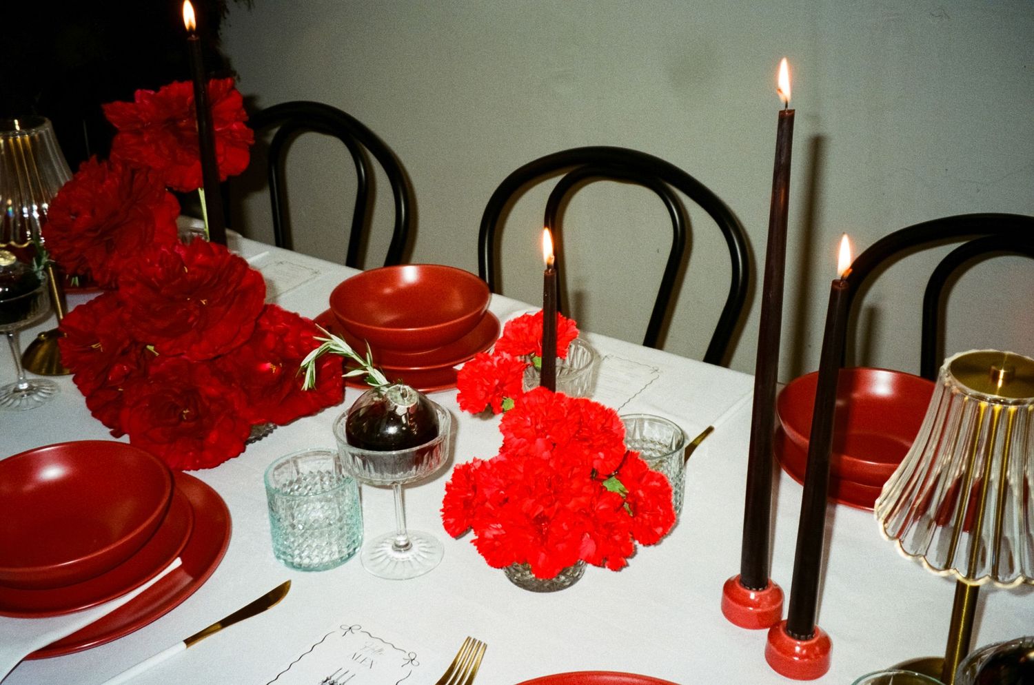 An elegant table setting with red carnation centerpieces, white candles and formal place settings.