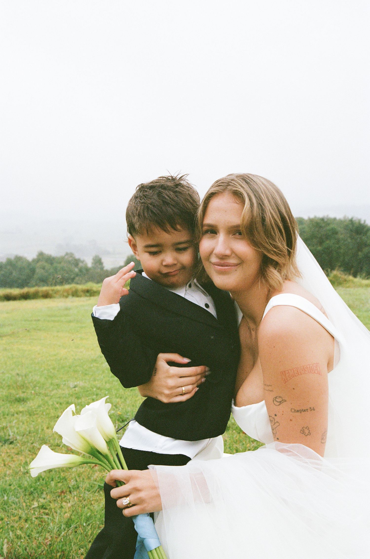 A tender moment captured in a grassy field with a white dress and black attire creating an intimate portrait.