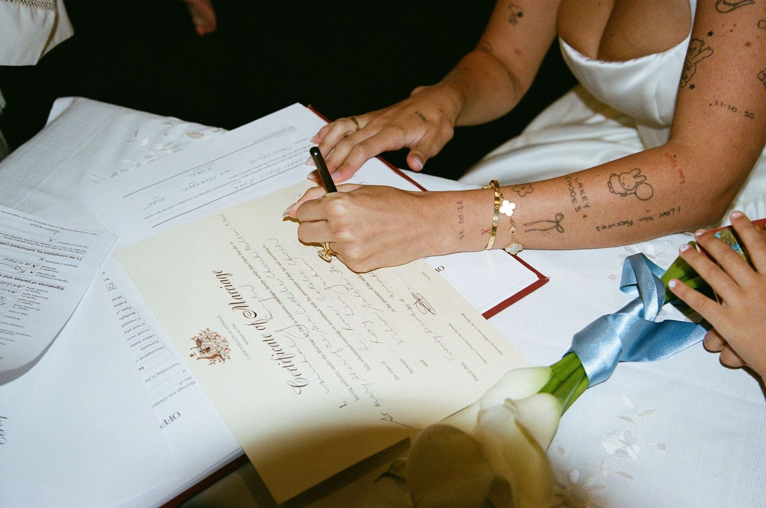 Close-up view of hands signing wedding documents with pens during a marriage ceremony.