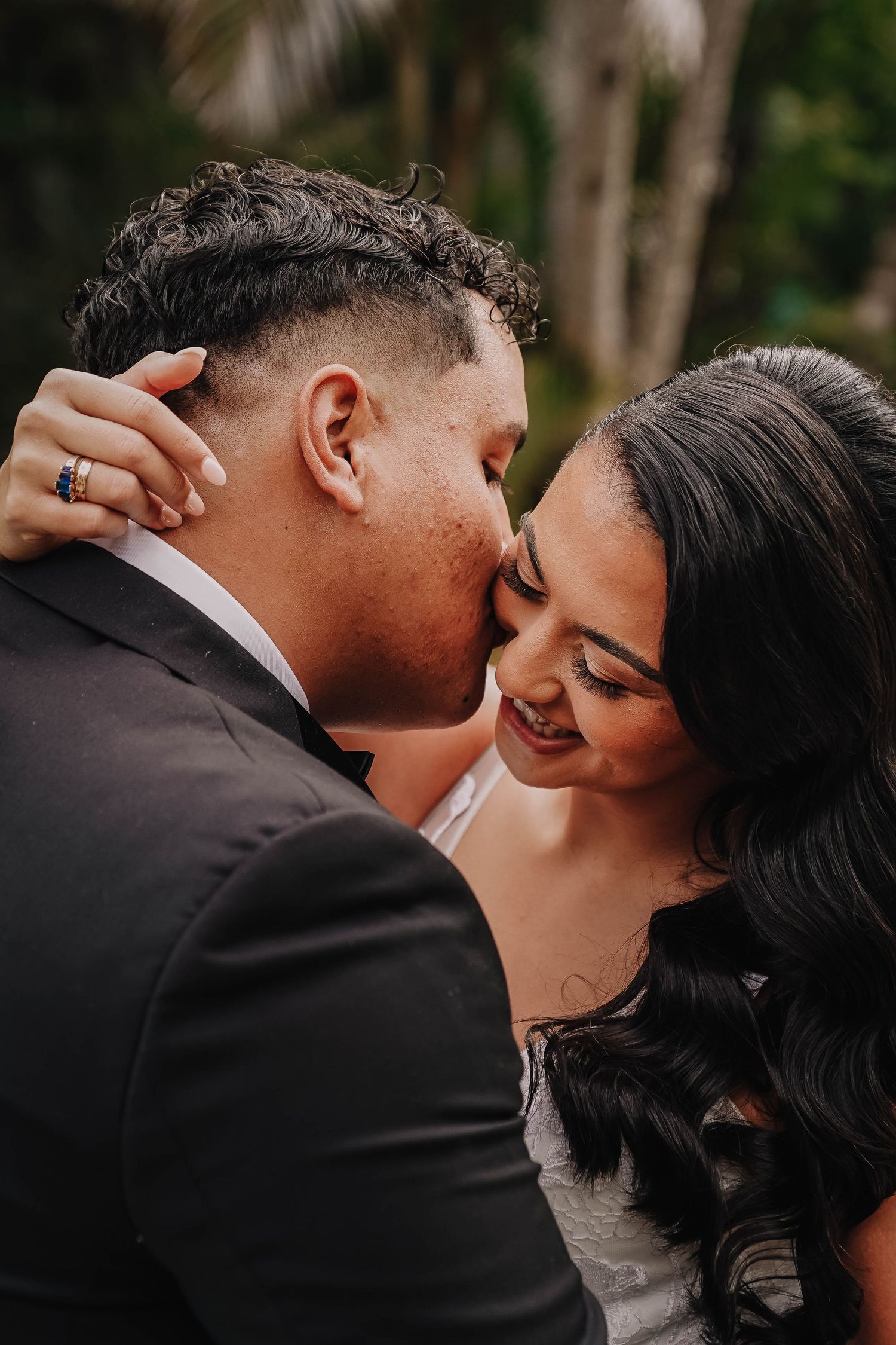 A tender moment between newlyweds in a romantic outdoor setting as they share intimate kisses against a natural backdrop.