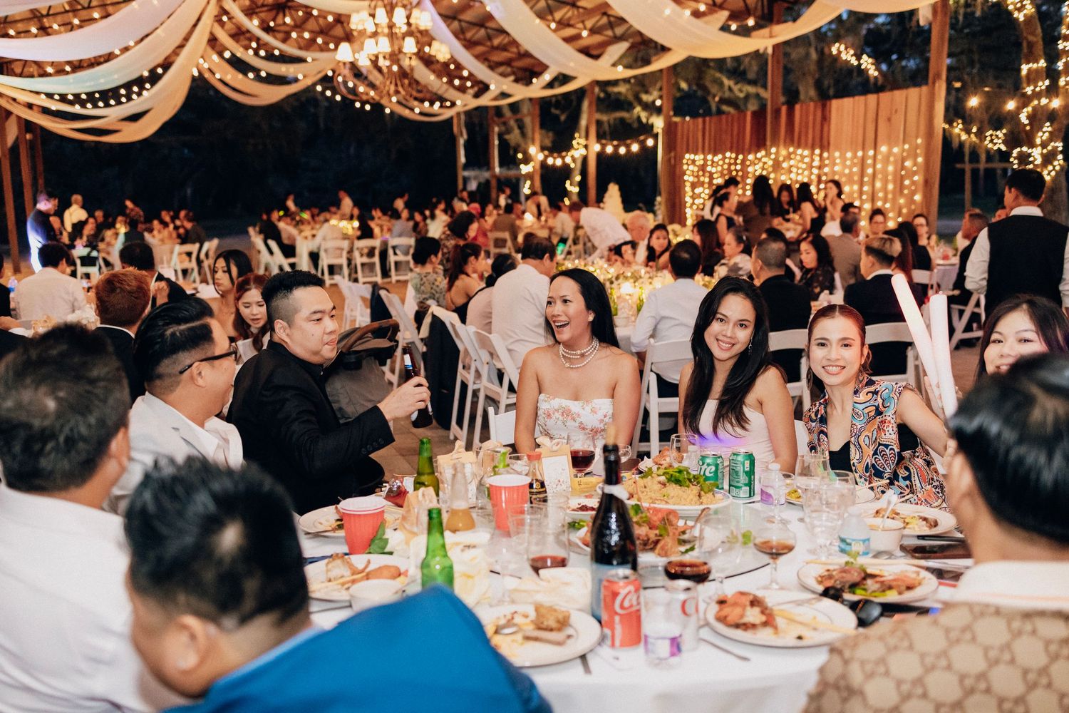 Guests laughing and dining together at an elegant outdoor wedding reception with string lights.