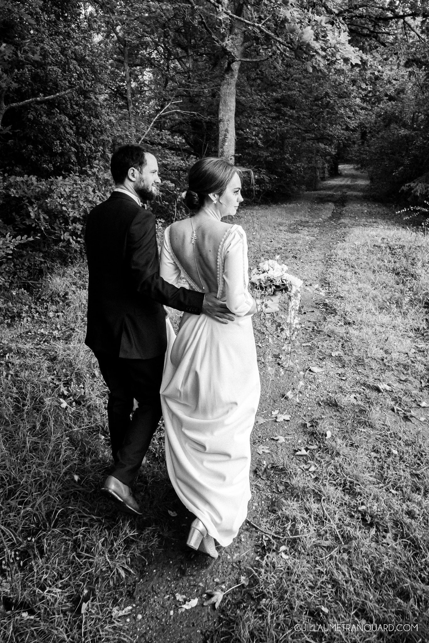Black and white series of romantic couple walking through wooded path during photo session.
