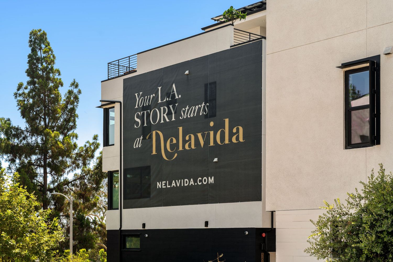 A large black and gold sign reading 'Your LA Story starts at Nelavida' mounted on a modern building exterior.