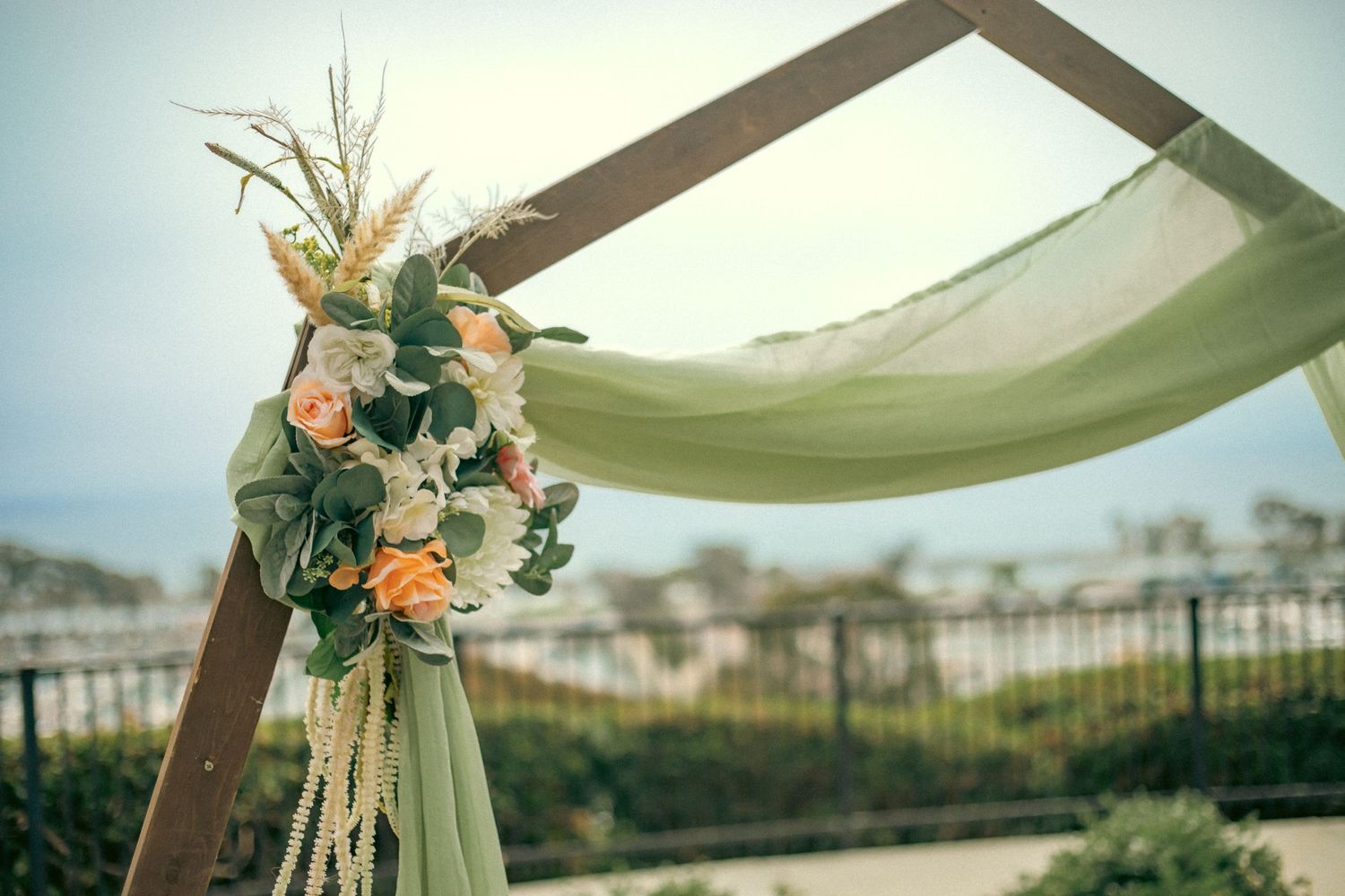 Wedding arch decorated with peach roses and greenery against a soft white fabric draping at an outdoor venue.