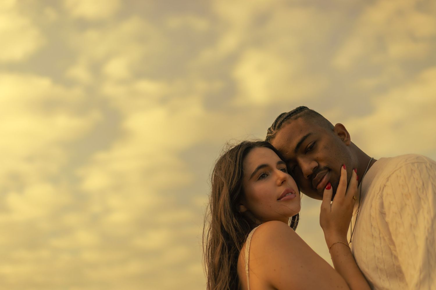 A romantic couple embraces during a golden sunset photoshoot in an outdoor setting.