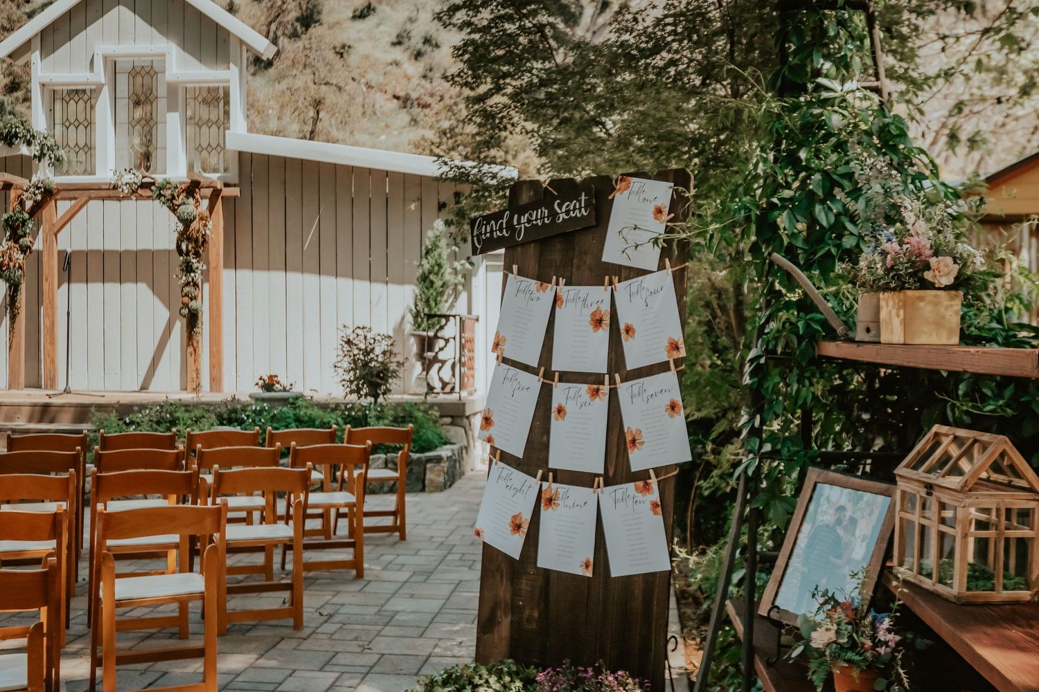 Rustic outdoor wedding setup in Southern California with wooden chairs and vintage decor display against white barn backdrop.