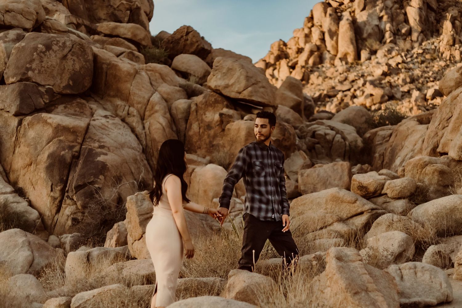 Romantic couple walking among large desert rock formations at sunset in Joshua Tree National Park for their engagement session