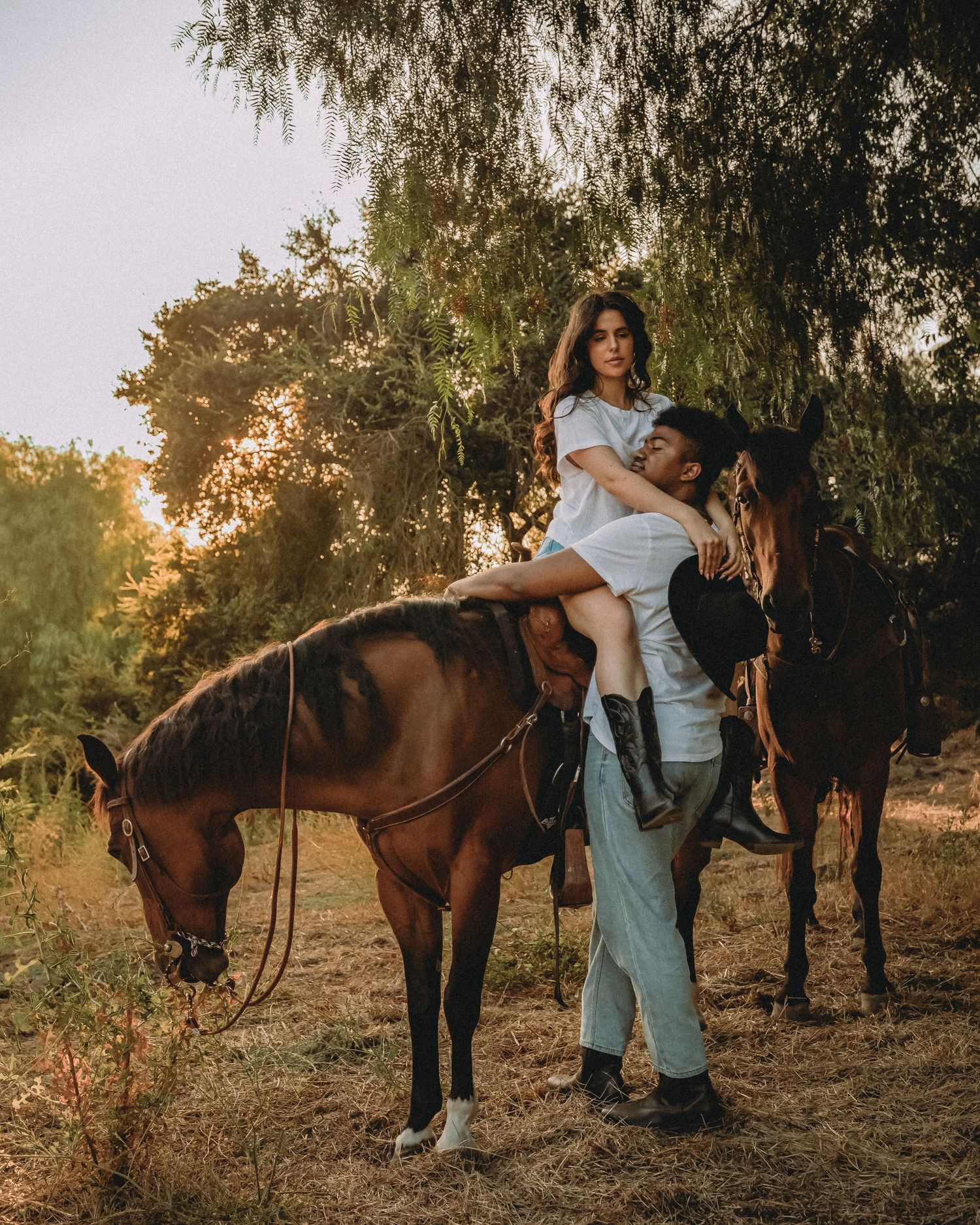 A SoCal couple poses with their brown horse during a golden sunset photoshoot on a farm.
