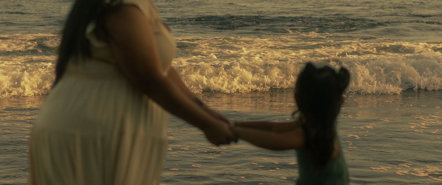 Two people stand together on a beach at sunset as gentle waves roll in along the shoreline.