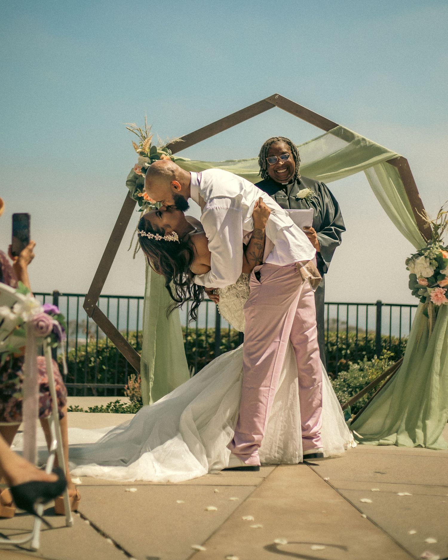 A joyful celebration at the outdoor wedding ceremony in Dana Point, California under a decorated archway with floral arrangements.