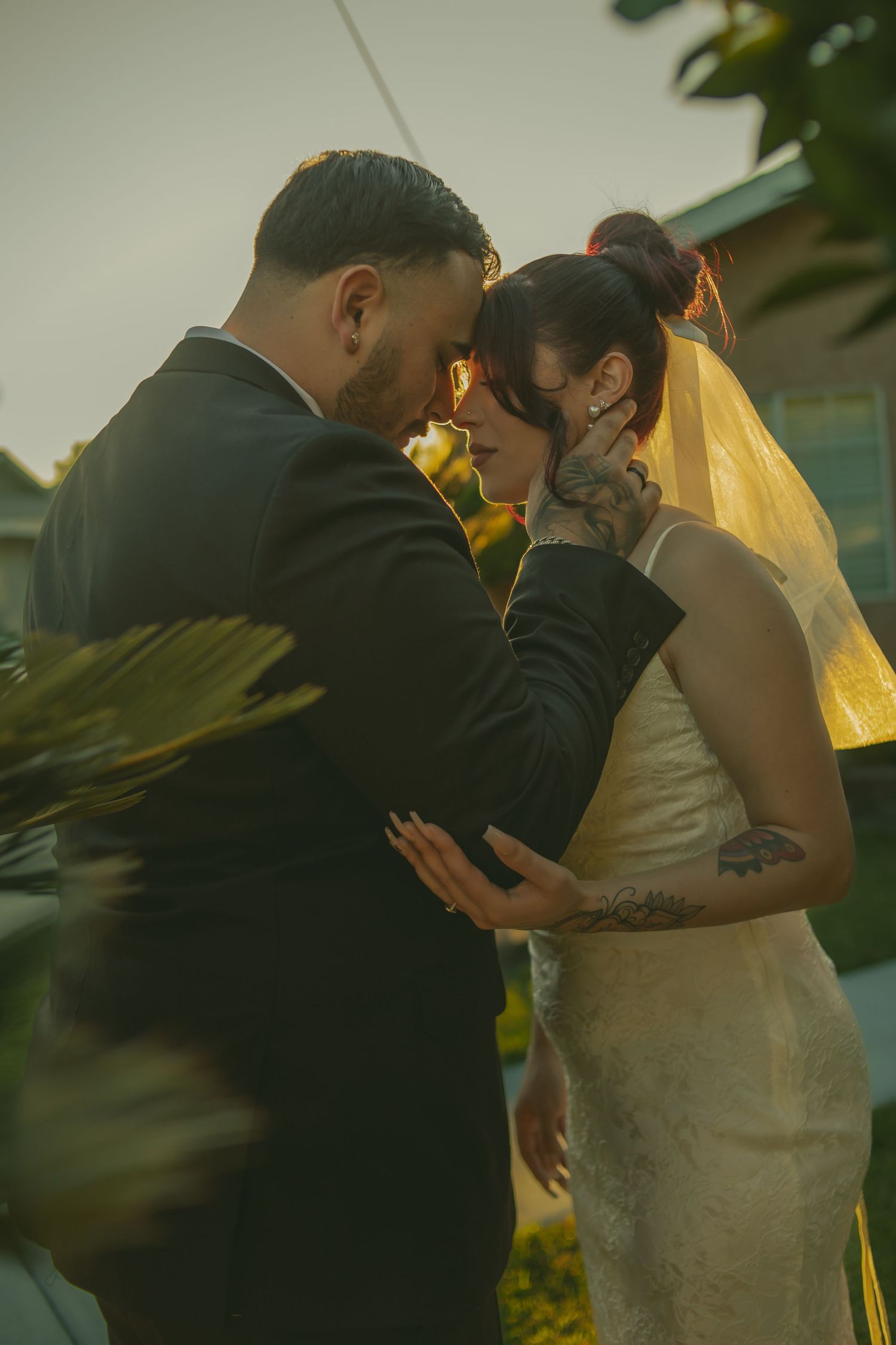 A couple shares an intimate moment in wedding attire during a sunset ceremony with a yellow glow shining through bride's veil.