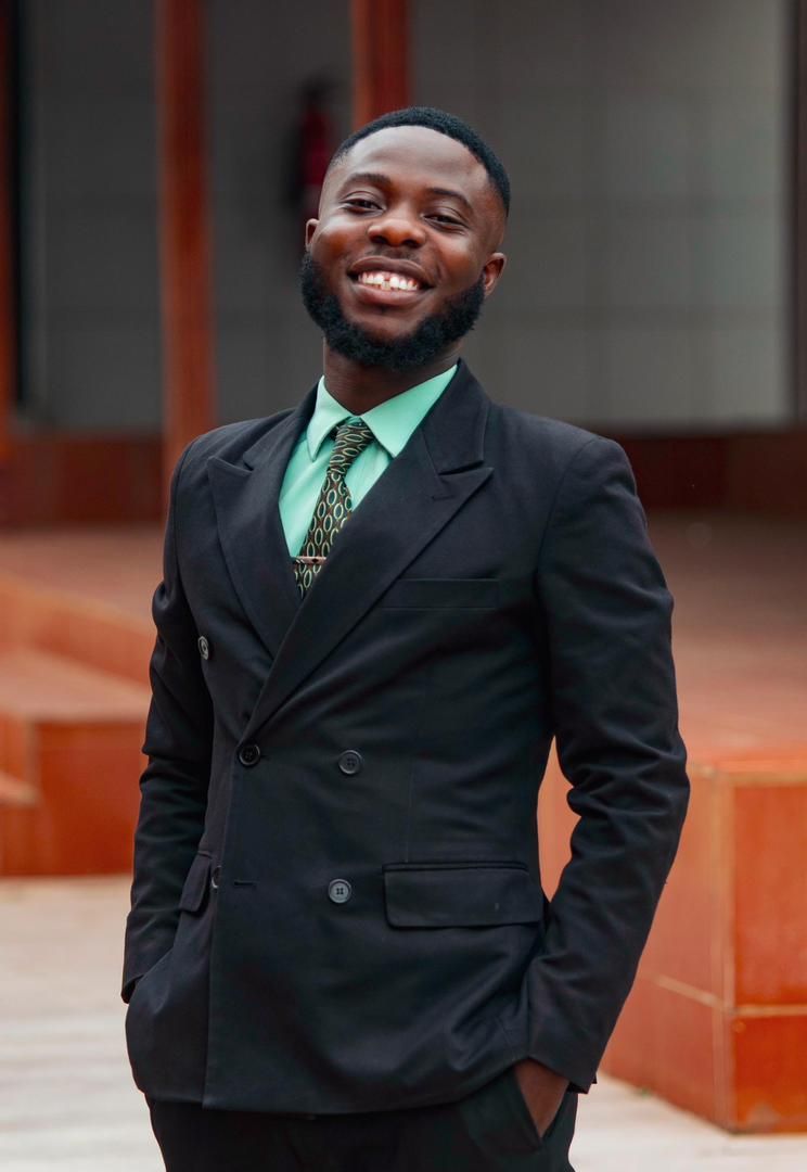 A formal portrait in a black suit and green tie against an architectural background.
