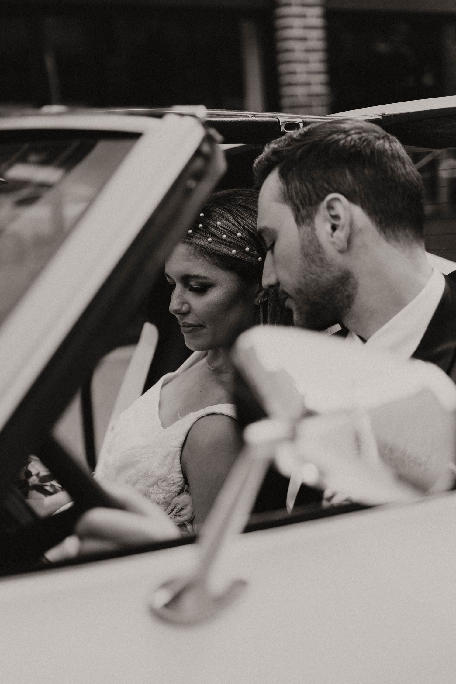 Black and white photo of a couple sharing an intimate moment in their wedding car.