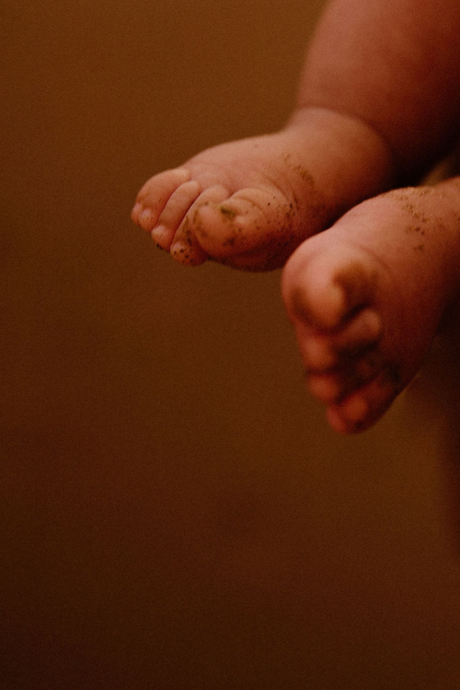 Close-up photo of tiny baby feet against a warm brown background in soft lighting during a newborn photoshoot in Wickham, WA