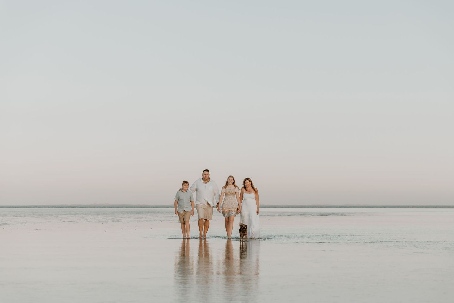 A family of four walk through the shallow water on a low tide at Hearsons Cove during a family photography session.