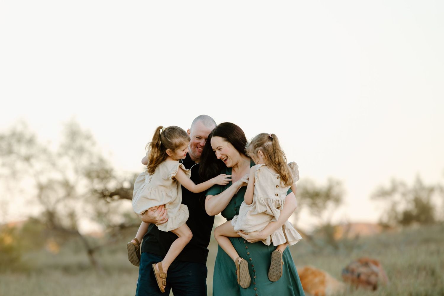 A family shares a tender moment together while standing in a golden sunlit field at sunset. Located in Cossack, WA