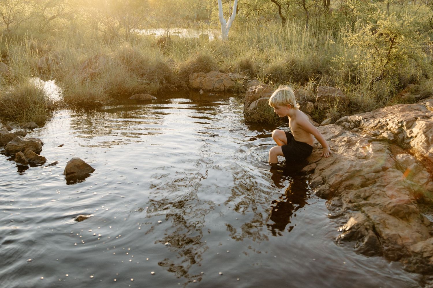 A young boy plays in a Rockpool in a river during a family photography session in Roebourne, WA