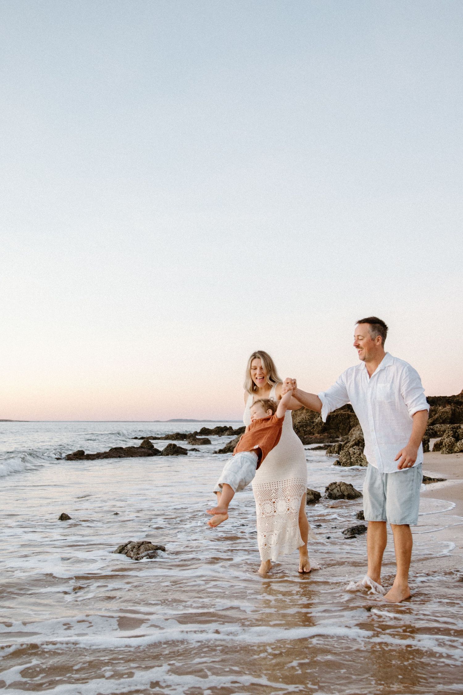 Parents swing their young child into the air during a maternity photoshoot in Wickham, WA