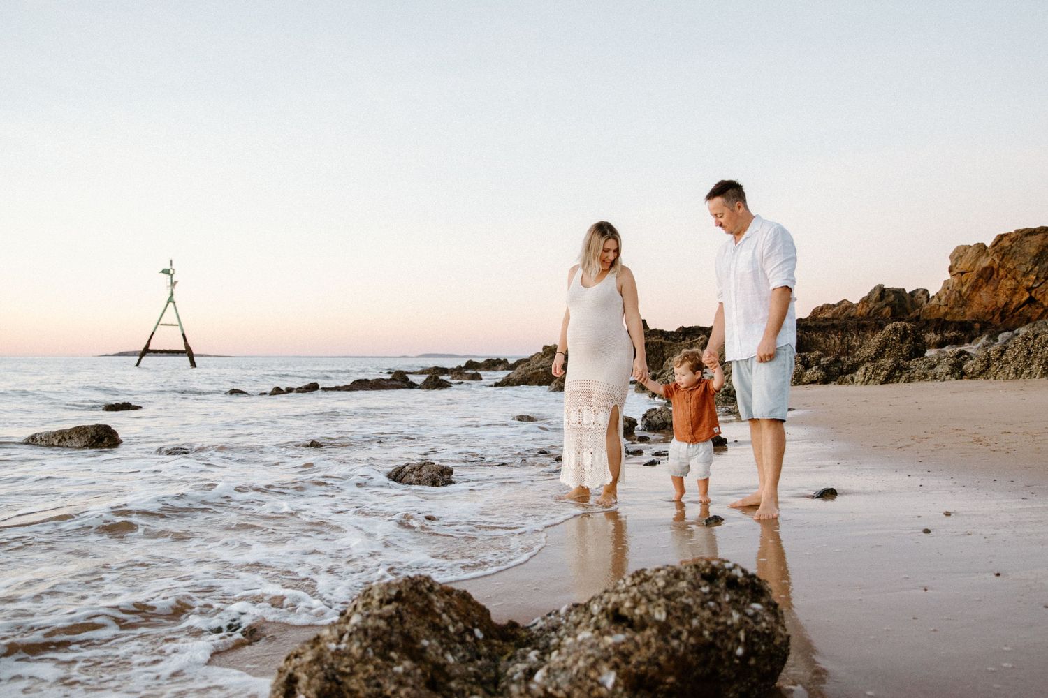 A family walks together along a rocky beach at sunset with waves crashing against the shore. Located in Point Samson, WA
