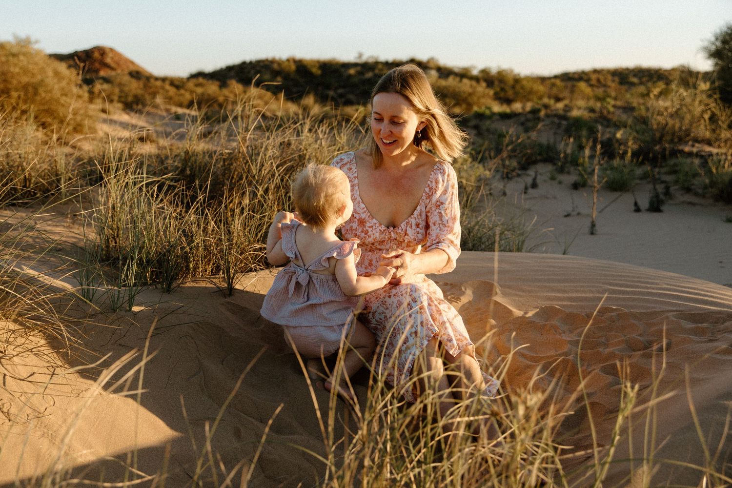 Motherhood photography session amongst coastal sand dunes and beach grass during golden hour in Wickham, WA