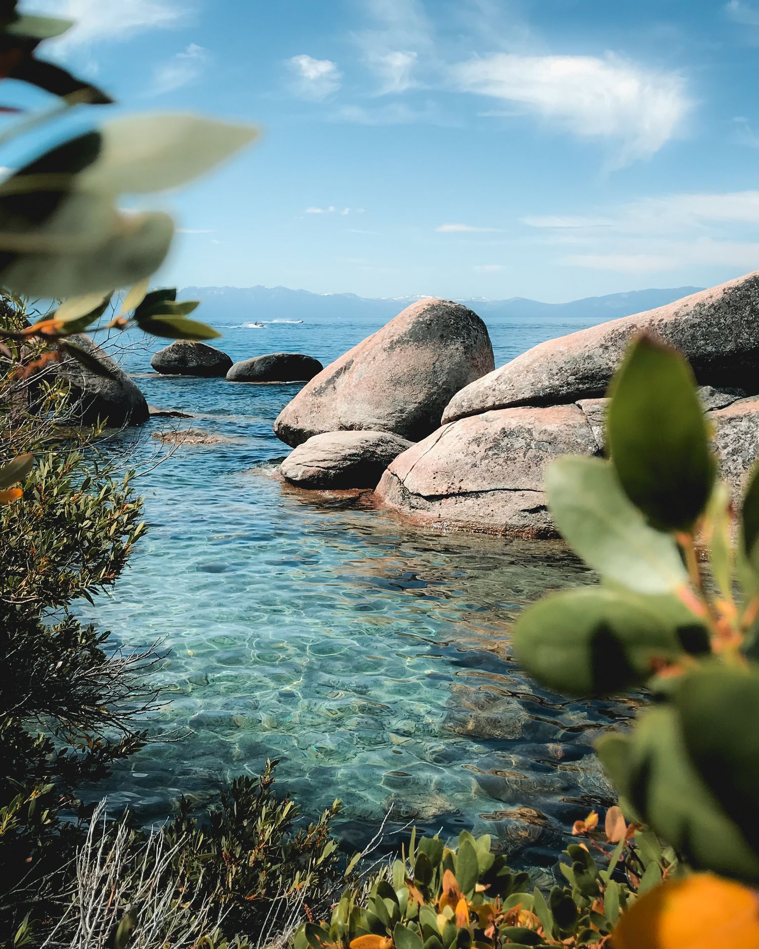Bright turquoise waters of Sand Harbor, Lake Tahoe, with a blue sky, green leaves, and granite boulders on a perfect summer day.