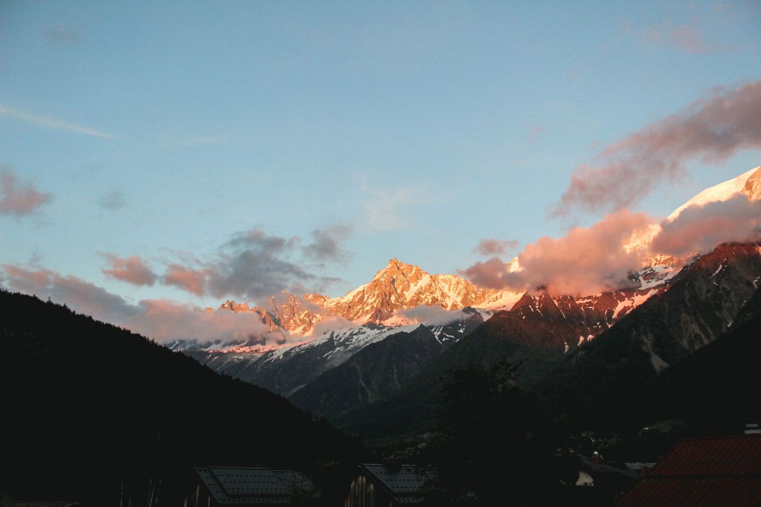 Panoramic view of Aiguille du Midi, Mont Blanc in Chamonix, France, featuring alpenglow on snow-covered peaks and orange sunset clouds.