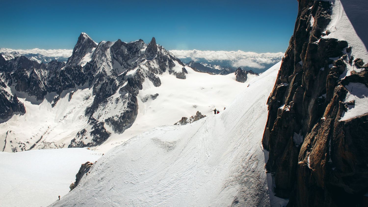 Panoramic view of La Vallée Blanche in Chamonix Mont Blanc, featuring snow-covered mountains, rocky terrain, and climbing mountaineers.