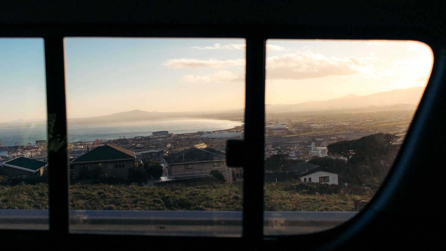 View of Cape Town, South Africa, by car. Sunrise, cape, bay, houses, travel, Africa, pale sky. Morning light, golden hour, clouds, blue sky.
