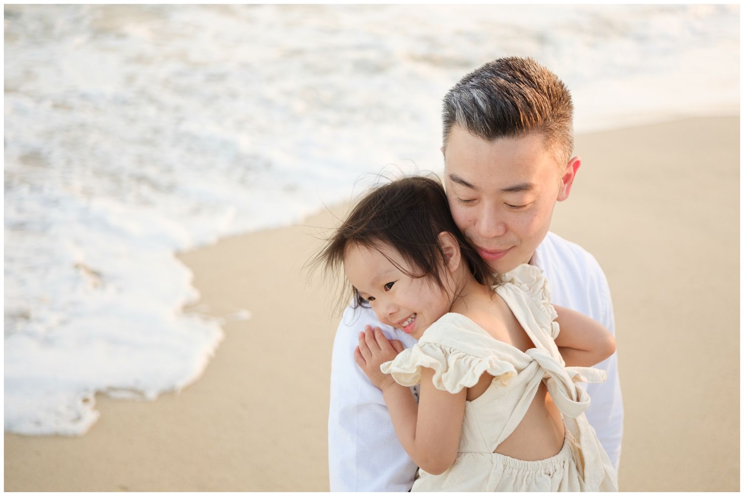 A loving parent and child share a tender moment together on a sandy beach as gentle waves roll in.