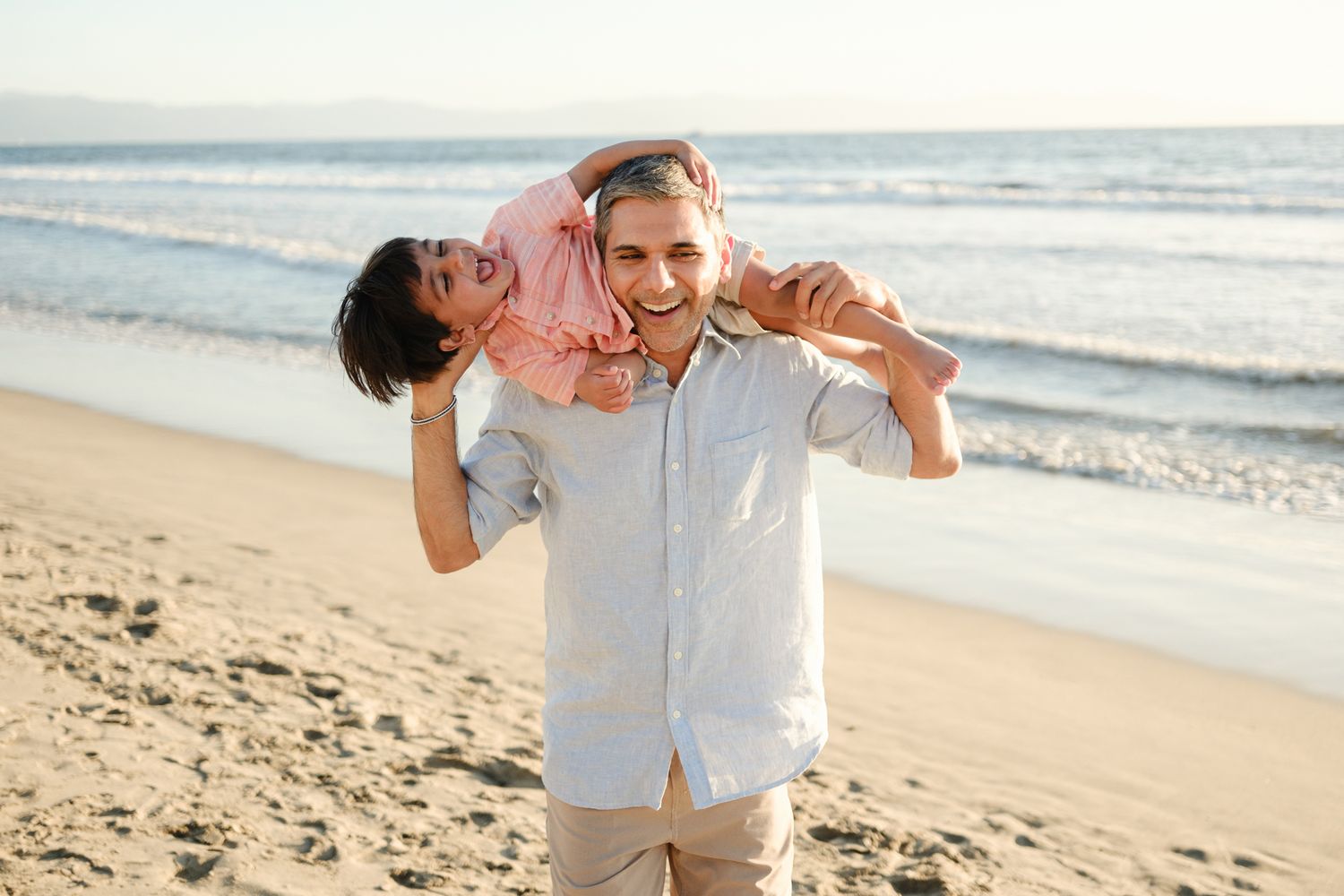 Playful piggyback ride along a sunny beach shoreline.