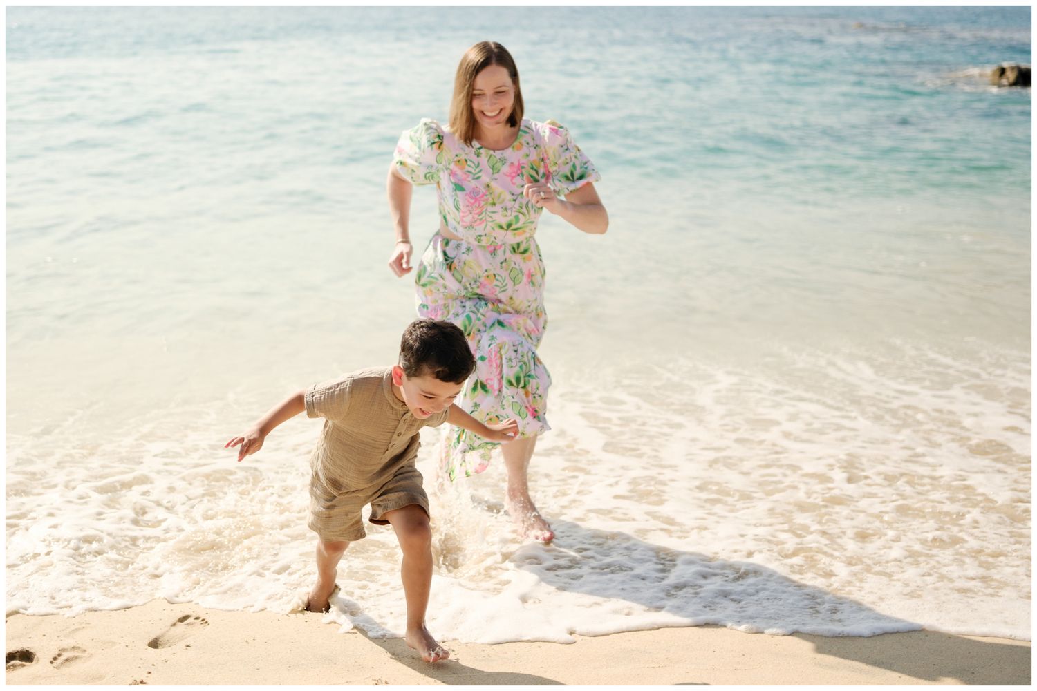 Two people run joyfully along a sunny beach with crystal clear turquoise water in the background.