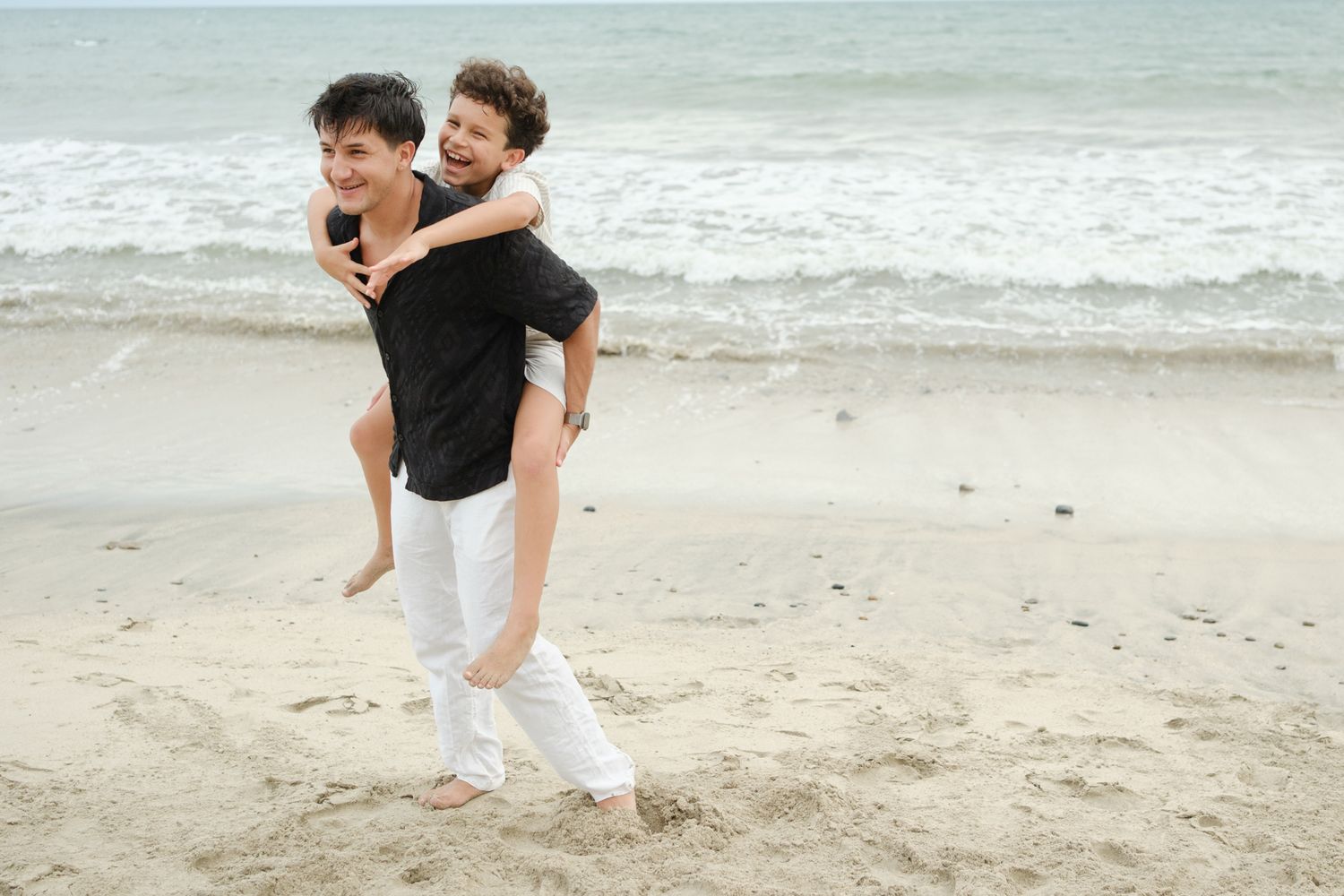 Two people having fun together on a beach with waves in the background.