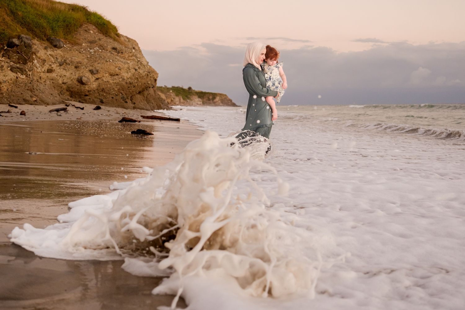 Figure standing in ocean waves during sunset with dramatic water splash.