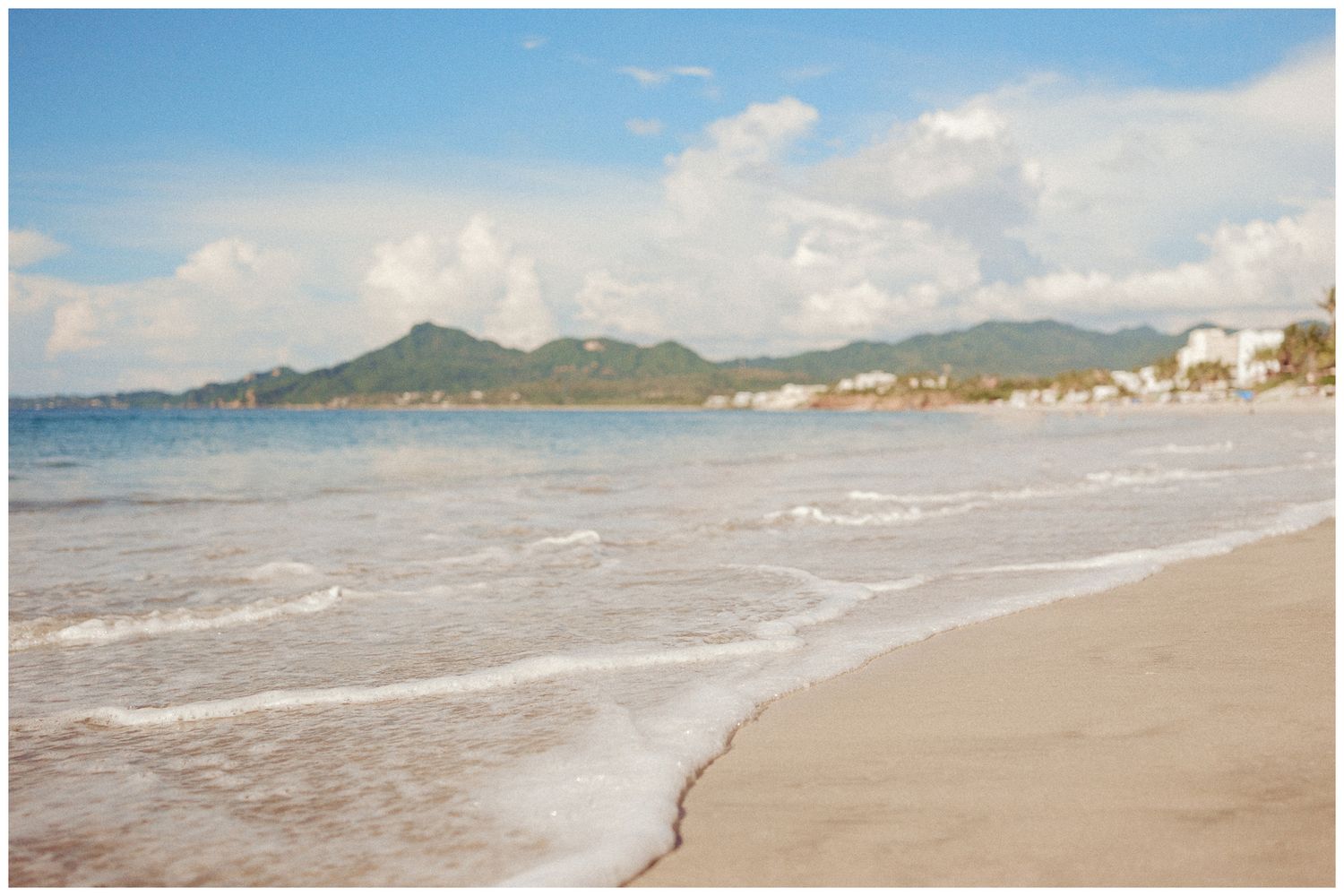 Panoramic view of a scenic coastal beach with distant mountains and gentle waves rolling onto sandy shores.