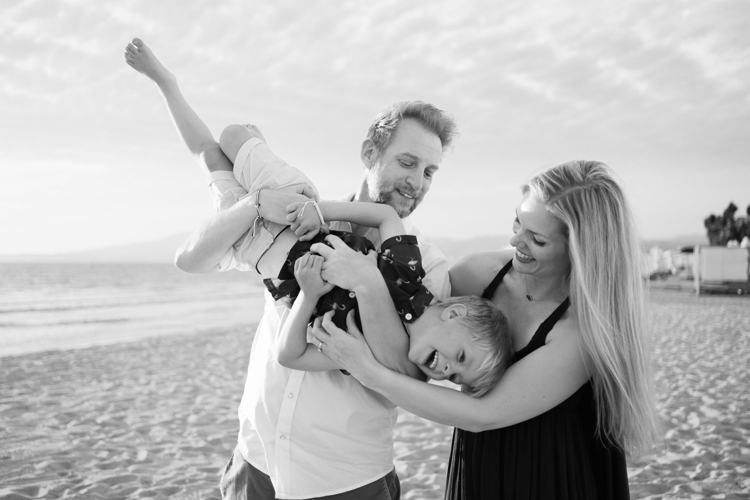 Black and white beach photoshoot series capturing intimate moments between a couple on a sunny day by the ocean.