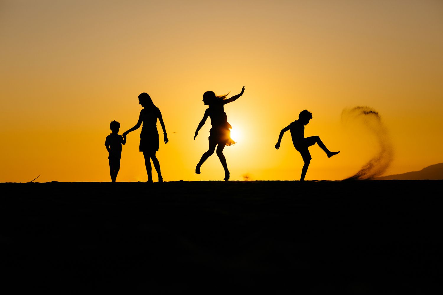Silhouettes of people dancing and jumping against a vibrant orange sunset sky.