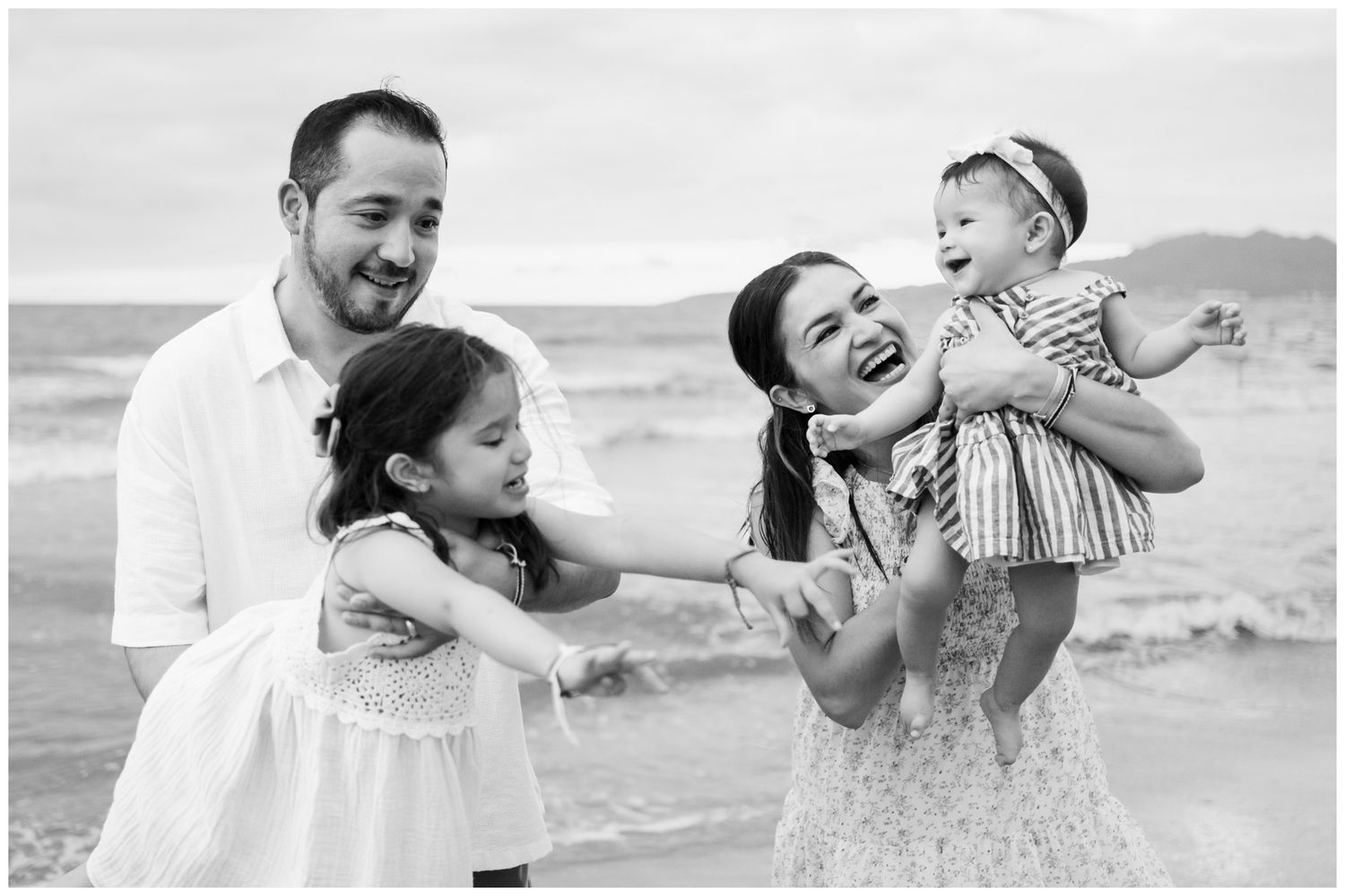 A joyful family shares candid laughter together during a black and white photo session at the beach.