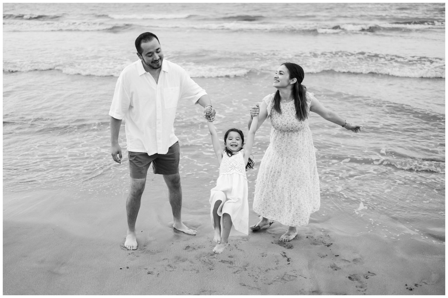 A family enjoying a beach day together in black and white as waves roll onto the shore.