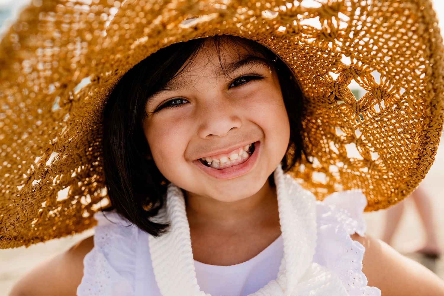 A bright expression shines under a woven straw sunhat with intricate lace-like patterns casting delicate shadows.
