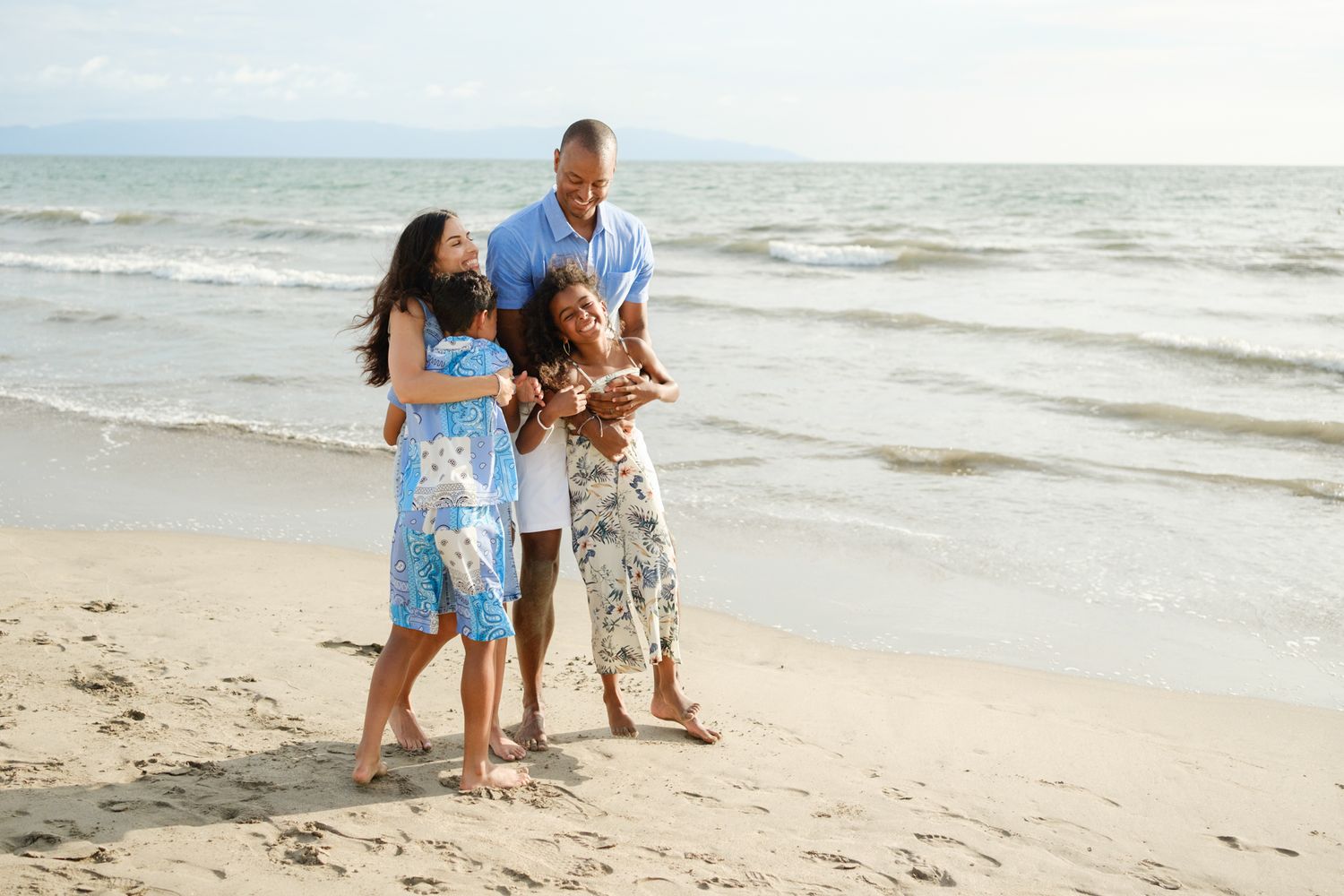 Family walking together on a sandy beach during a sunny day as waves crash against the shore.