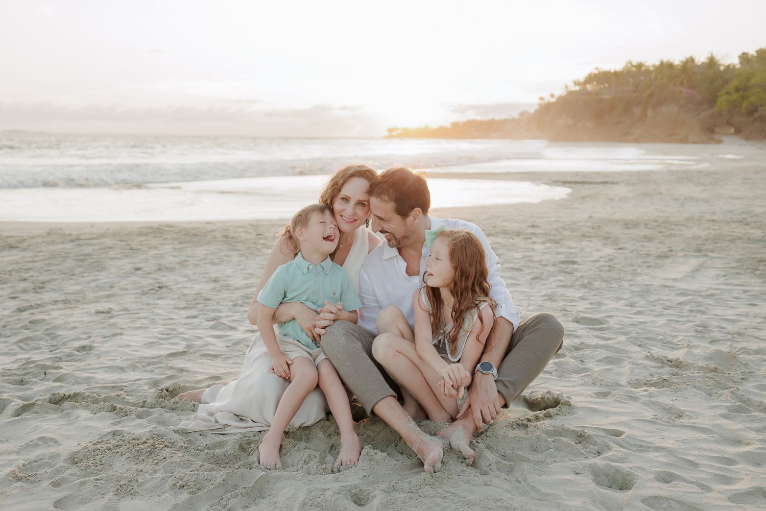 Family sitting together on a sandy beach at golden hour during a Punta Mita family photo session.