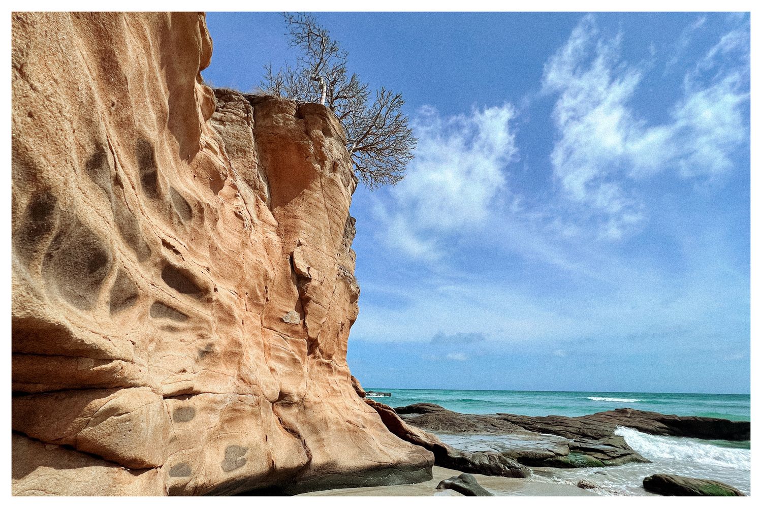 Aerial panoramic view of rugged coastal cliffs and crystal blue ocean waters along a tropical shoreline.