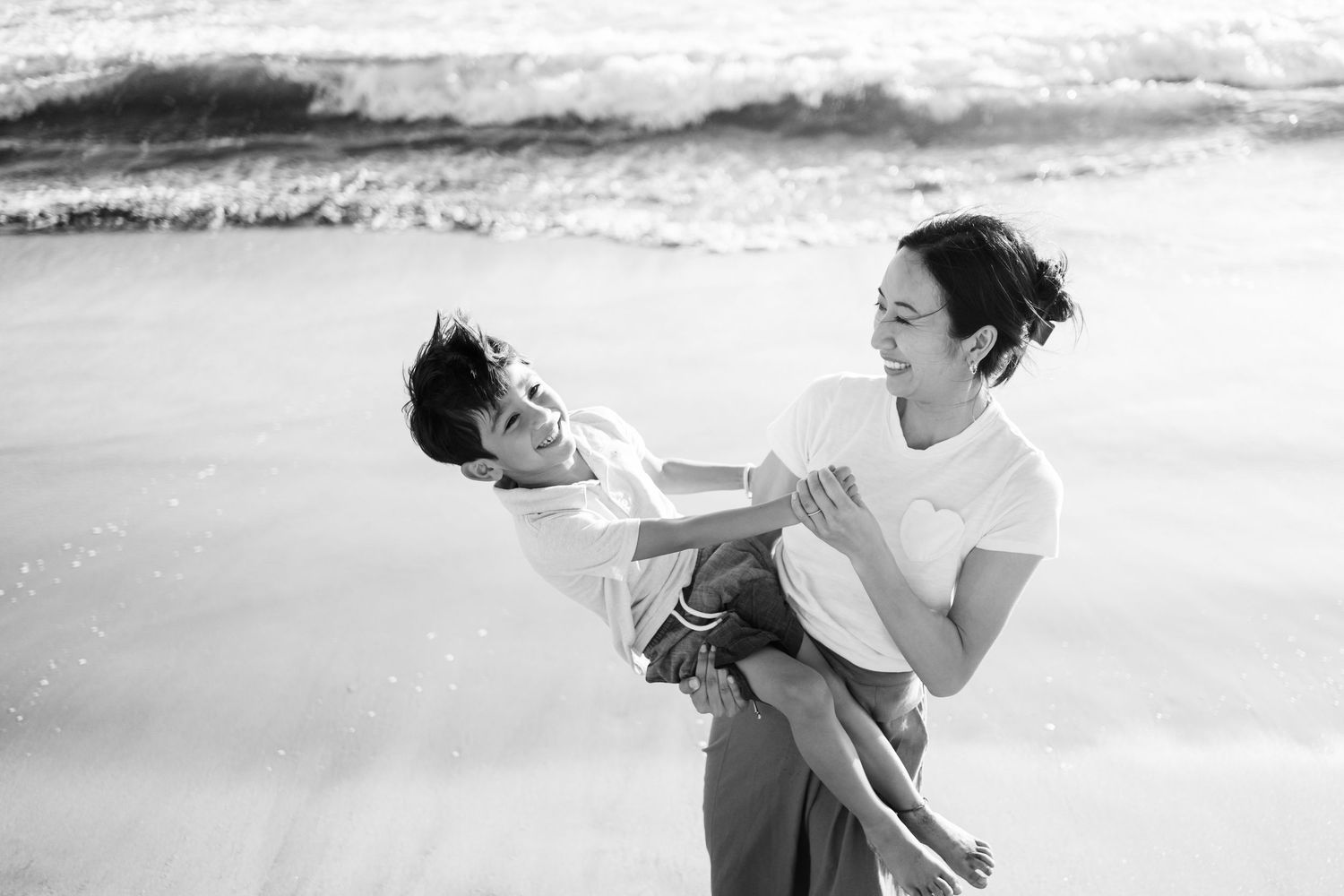 A couple embraces in black and white photography while dancing at the beach.