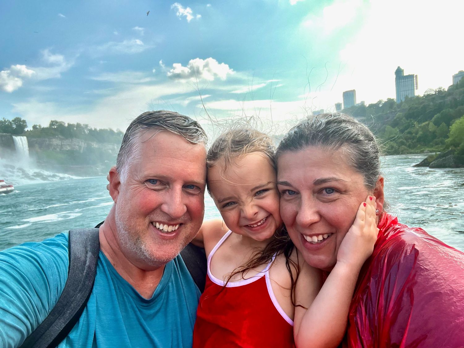 A group of people pose for selfies near Niagara Falls with mist and scenic views visible in the background.